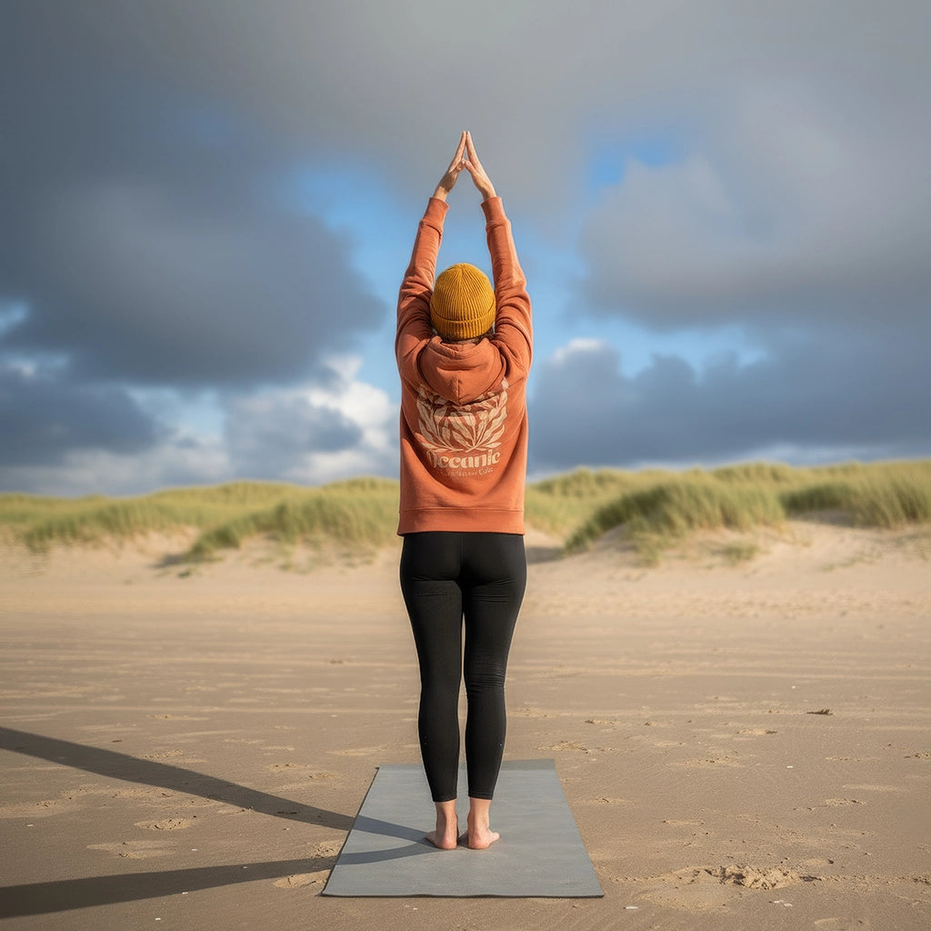 <img src="Oceanic-Club-Hoodie-heritage-brown-back-woman-Yoga-sport-mountain-pose_1024px.webp" alt="Frau in Mountain Pose am Strand, trägt den unisex Oceanic Club Hoodie in Heritage Brown: großer Algen-Backprint und kleiner Brustprint, gefertigt aus 100% GOTS-zertifizierter Bio-Baumwolle, meditative Yoga-Atmosphäre mit Dünenblick">