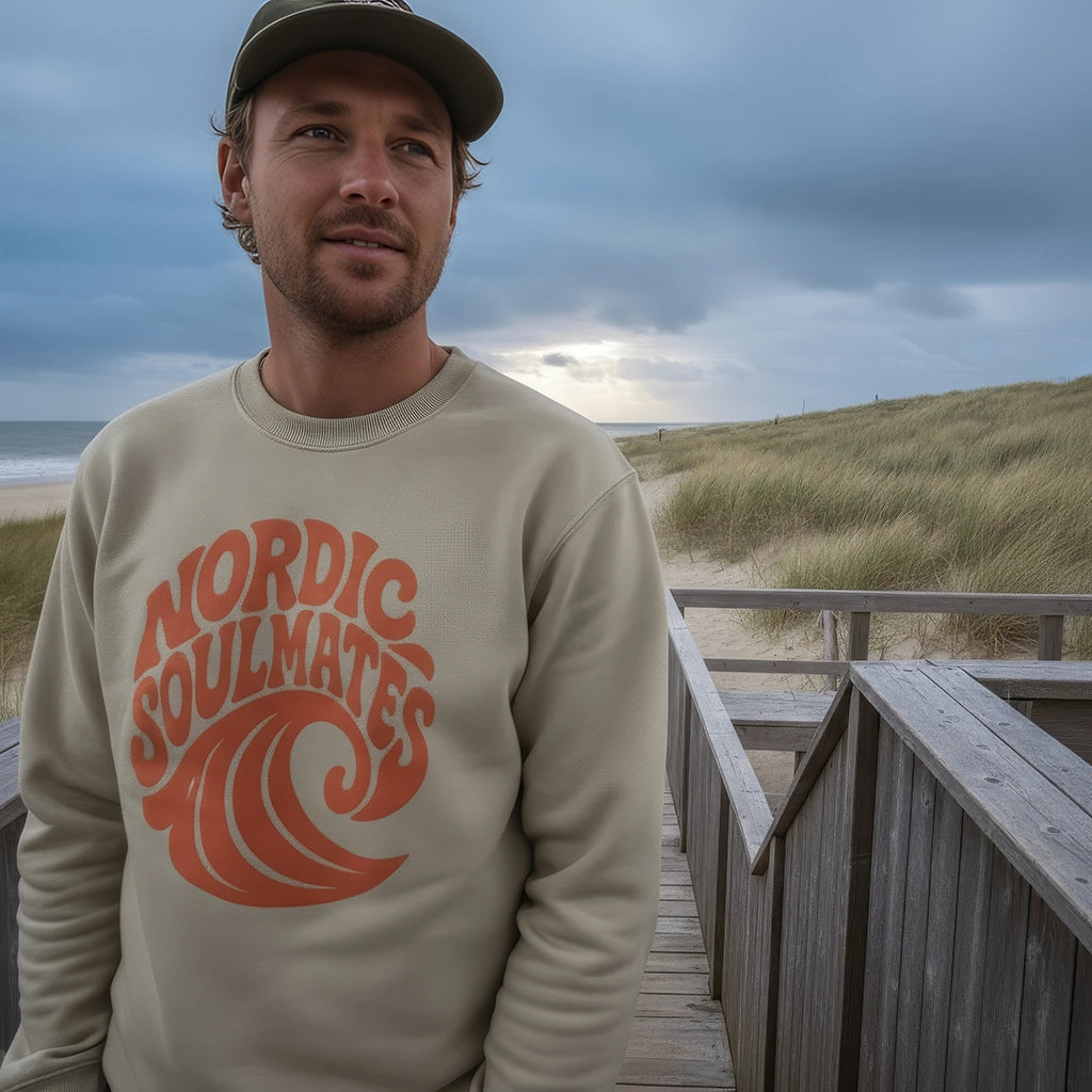 <img src="Tide-and-Time-Sweatshirt-stone-front-man-Beachclub-standing_1024px.webp" alt="Lächelnder Mann steht auf einem Steg zum Strandcafé, trägt das Tide and Time Sweatshirt in Stone: kreisförmiger Frontprint mit stilisierter Welle und Schriftzug 'Nordic Soulmates', Blick in die Ferne, maritime Atmosphäre mit Dünen im Hintergrund, gefertigt aus 100% GOTS-zertifizierter Bio-Baumwolle">