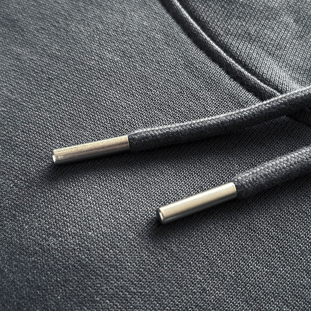 <img src="Unity-Circle-Hoodie-India-Ink-Grey-Detail-Textur-Kordel-Naht_1024px.webp" alt="Detailaufnahme eines india ink grey Hoodies: feine Struktur der gekämmten, ringgesponnenen Bio-Baumwolle, präzise Doppelnaht-Steppstiche an Ärmelbündchen und Saum, hochwertige Kordeln mit Metallenden, gefertigt aus 100% GOTS-zertifizierter Bio-Baumwolle">