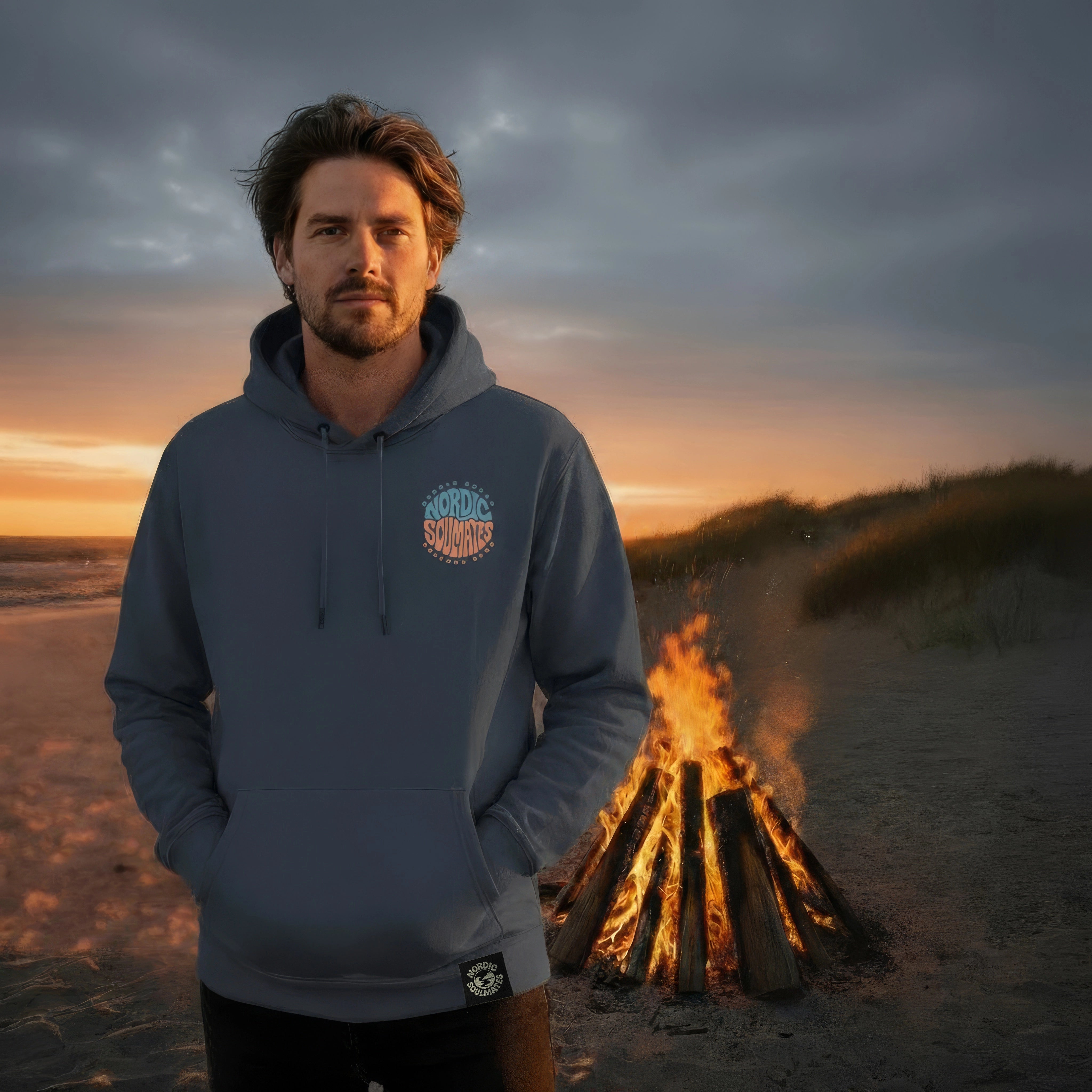 <img src="nordic-soulmates-unity-circle-hoodie-india-ink-grey-men-lagerfeuer-strand-frontal.jpg" alt="Mann am Lagerfeuer am Strand trägt den Unisex Nordic Soulmates Unity Circle Hoodie in India Ink Grey: Frontalansicht mit Blick in die Kamera, minimalistischer Brustprint im Fokus, umspielt von warmem Feuerlicht und natürlicher Küstenatmosphäre, gefertigt aus 100% GOTS-zertifizierter Bio-Baumwolle">