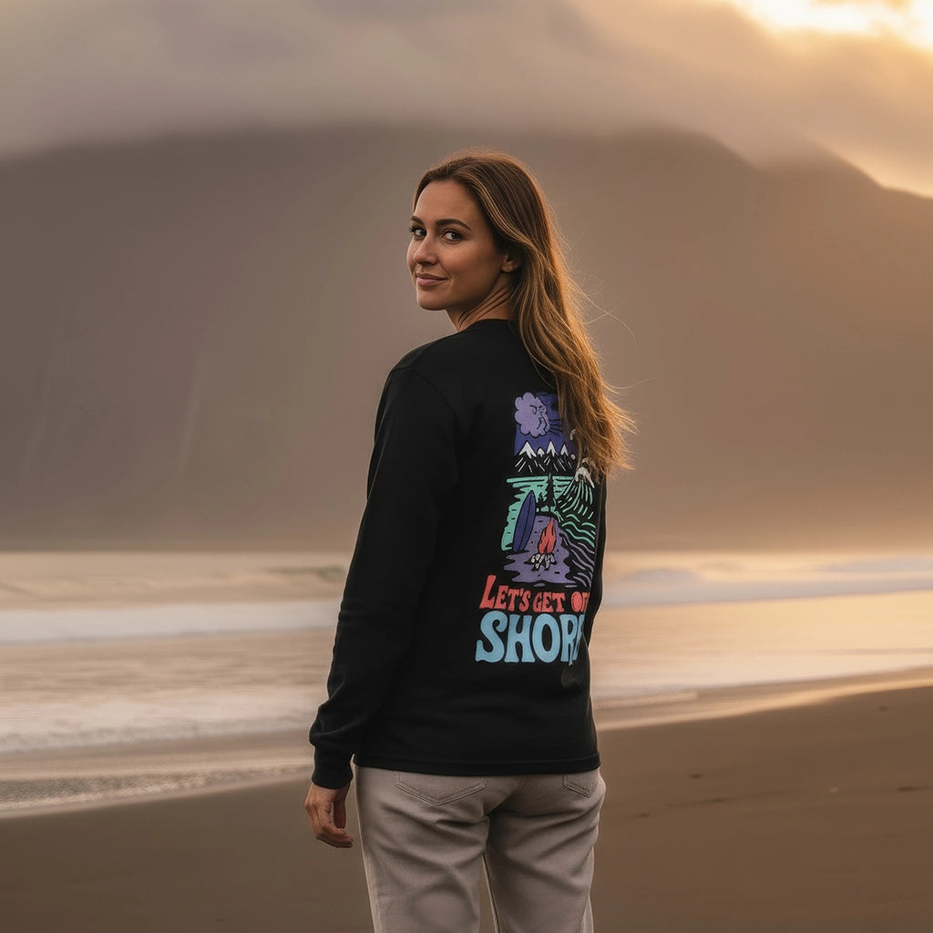 <img src="lets-get-offshore-longsleeve-black-frau-rueckansicht-schwarzer-sandstrand-vulkan.webp" alt="Frau trägt das 'Let’s Get Offshore' Longsleeve in Black: Rückansicht mit Blick über die Schulter in die Kamera, großer Backprint mit nordischer Landschaft und Surfer-Symbolik, schwarzer Sandstrand und dramatischer Vulkan im Hintergrund, gefertigt aus 100% GOTS-zertifizierter Bio-Baumwolle">