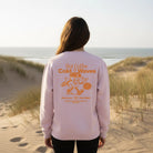 <img src="Hot-Coffee-Cold-Waves-Sweatshirt-cotton-pink-back-Woman-beach_1024px.webp" alt="Close-Up einer Frau in den Dünen am Strand, trägt das Hot Coffee Cold Waves Sweatshirt in Cotton Pink: Rückansicht mit großem orangefarbenem Backprint, maritimes Design, natürliche Küstenatmosphäre, gefertigt aus 100% GOTS-zertifizierter Bio-Baumwolle">