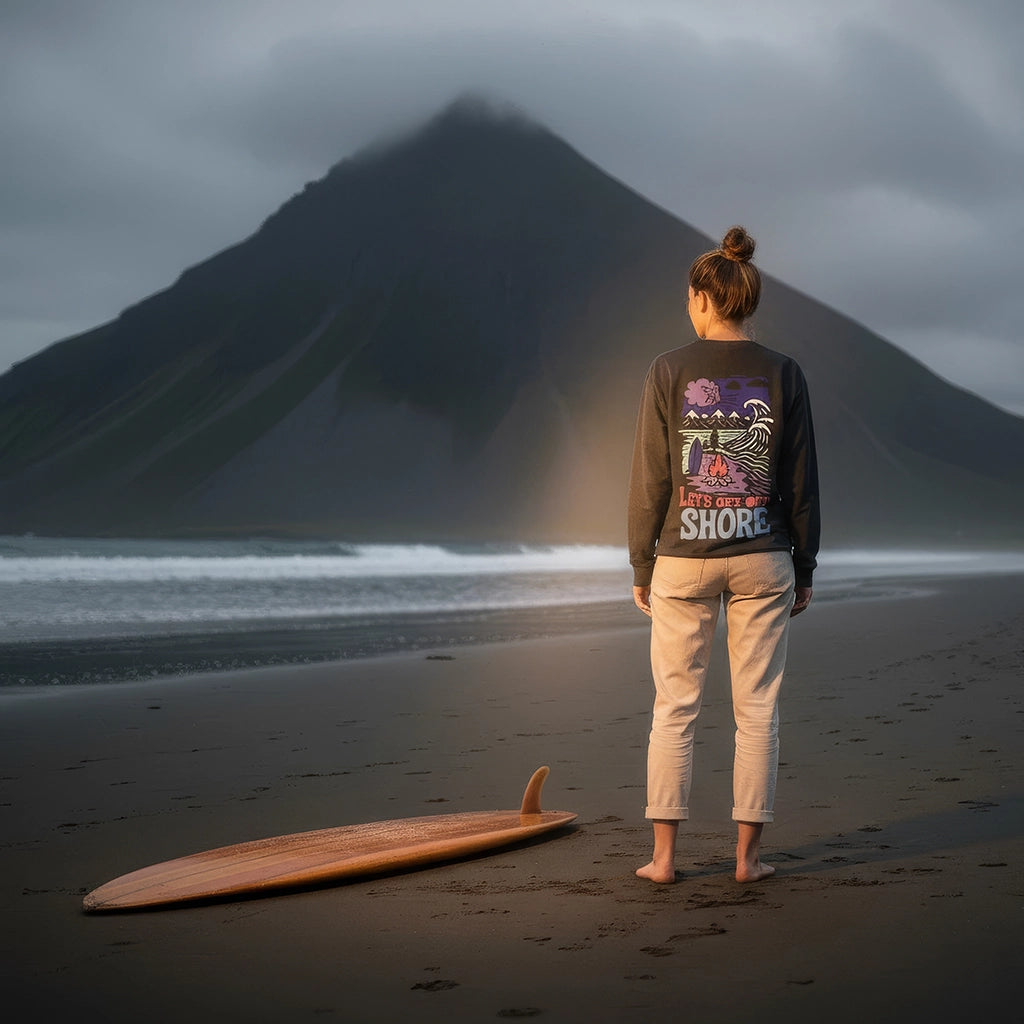 <img src="Lets-Get-Offshore-Longsleeve-Black-Backprint-Woman-Black-Beach-Close_1024px.webp" alt="Frau am schwarzen Sandstrand im 'Let’s Get Offshore' Longsleeve in Black: Rückansicht mit großem Backprint einer nordischen Landschaft und Surfer-Symbolik, dramatischer dunkler Berg im Hintergrund, gefertigt aus 100% GOTS-zertifizierter Bio-Baumwolle">