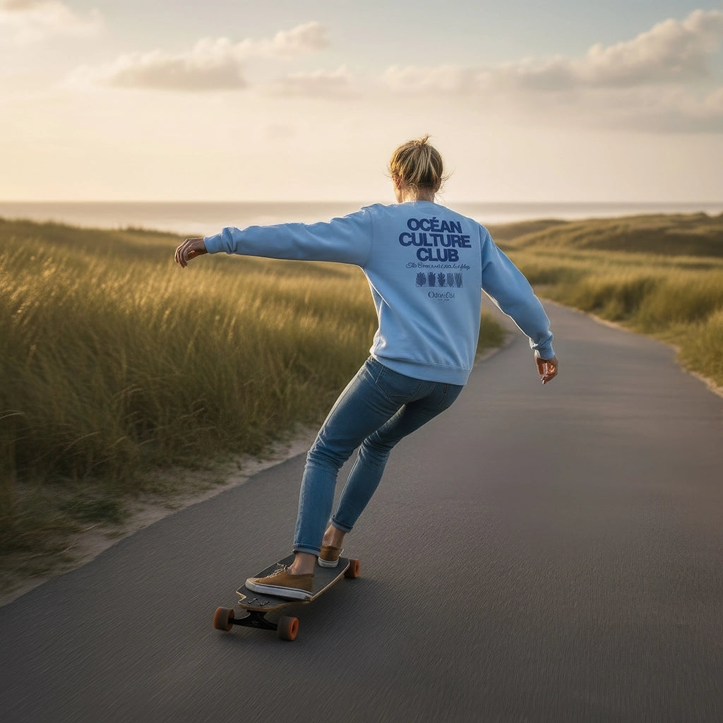 <img src="Ocean-Culture-Club-Sweatshirt-blue-soul-back-woman-carving-Longboard-1024px.webp" alt="Frau carvt entspannt auf dem Longboard am Strand, trägt das Ocean Culture Club Sweatshirt in Blue Soul (hellblau): Rückansicht mit großem Backprint (Schriftzug 'Ocean Culture Club' und gradlinige Illustrationen von Wasserpflanzen, Algen und Korallen), maritime Atmosphäre, gefertigt aus 100% GOTS-zertifizierter Bio-Baumwolle">