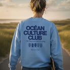 <img src="Ocean-Culture-Club-Sweatshirt-blue-soul-back-woman-walking-Longboard-1024px.webp" alt="Frau in den Dünen mit Longboard unter dem Arm, trägt das Ocean Culture Club Sweatshirt in Blue Soul (hellblau): Close-Up des großen Backprints mit Schriftzug 'Ocean Culture Club' und gradlinigen Illustrationen von Wasserpflanzen, Algen und Korallen darunter, Blick in die Ferne, entspannte Küstenatmosphäre, gefertigt aus 100% GOTS-zertifizierter Bio-Baumwolle">