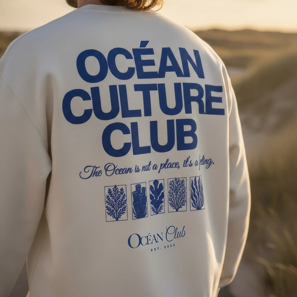 <img src="Ocean-Culture-Club-Sweatshirt-off-white-back-man-walking-Longboard-1024px.webp" alt="Close-Up eines Mannes in den Dünen (unscharf im Hintergrund), trägt das Ocean Culture Club Sweatshirt in Off-White: Fokus auf den großen Backprint mit Schriftzug 'Ocean Culture Club' und gradlinigen Illustrationen von Wasserpflanzen, Algen und Korallen, entspannte Küstenatmosphäre, gefertigt aus 100% GOTS-zertifizierter Bio-Baumwolle">