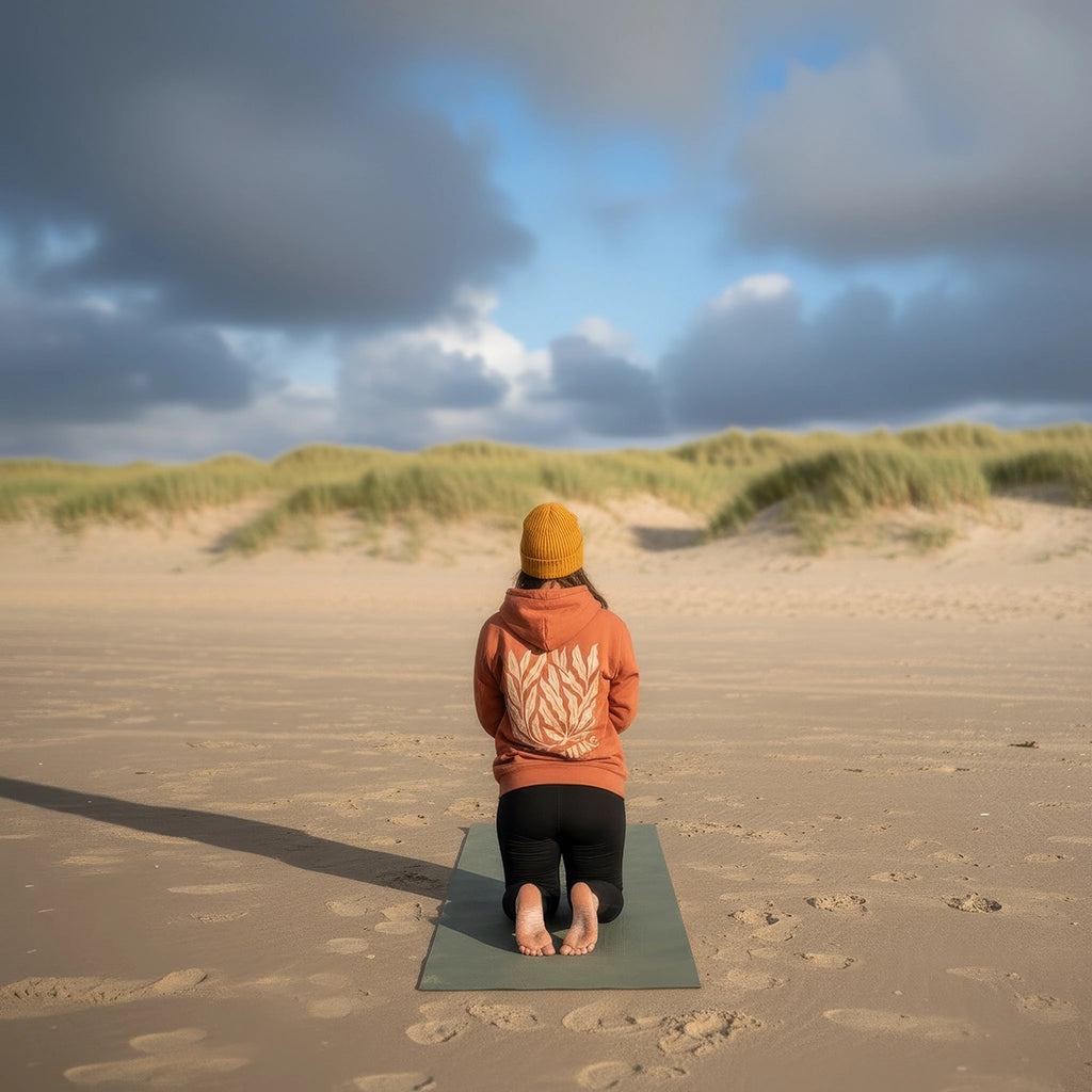 <img src="Oceanic-Club-Hoodie-heritage-brown-back-woman-Yoga-meditation_1024px.webp" alt="Frau in meditativer Haltung am Strand, trägt den unisex Oceanic Club Hoodie in Heritage Brown: großer Algen-Backprint, ruhige Konzentration mit Meerblick, gefertigt aus 100% GOTS-zertifizierter Bio-Baumwolle">
