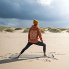 <img src="Oceanic-Club-Hoodie-heritage-brown-back-woman-Yoga-sport-high-lunge_1024px.webp" alt="Frau in High Lunge am Strand, trägt den unisex Oceanic Club Hoodie in Heritage Brown: großer Algen-Backprint, dynamische Yoga-Pose mit Meerblick, gefertigt aus 100% GOTS-zertifizierter Bio-Baumwolle">