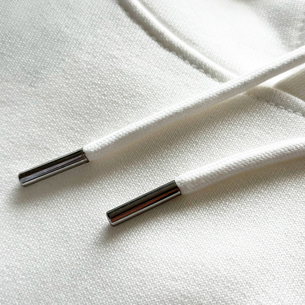 <img src="weisser-hoodie-struktur-biobaumwolle-doppelnaht-kordeln-detail.jpg" alt="Detailaufnahme eines weißen Hoodies: feine Struktur der gekämmten, ringgesponnenen Bio-Baumwolle, präzise Doppelnaht-Steppstiche an Ärmelbündchen und Saum, hochwertige Kordeln mit Metallenden, gefertigt aus 100% GOTS-zertifizierter Bio-Baumwolle">