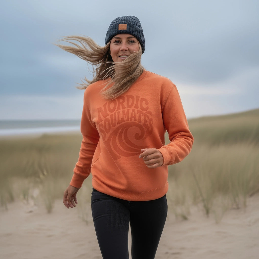<img src="Tide-and-Time-Sweatshirt-fiesta-front-woman-Beach-running_1024px.webp" alt="Frau läuft entspannt am Strand entlang, trägt das Tide and Time Sweatshirt in Fiesta (rot-orange) mit kreisförmigem Frontprint: stilisierte Welle und Schriftzug 'Nordic Soulmates', Dünen im Hintergrund, aktive Küstenatmosphäre, gefertigt aus 100% GOTS-zertifizierter Bio-Baumwolle">