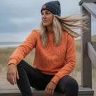 <img src="Tide-and-Time-Sweatshirt-fiesta-front-woman-Beachclub-sitting_1024px.webp" alt="Frau sitzt auf der Holztreppe eines Beachclubs, trägt das Tide and Time Sweatshirt in Fiesta (rot-orange) mit kreisförmigem Frontprint: stilisierte Welle und Schriftzug 'Nordic Soulmates', entspannte Pose mit Beanie, Dünen im Hintergrund, maritime Atmosphäre, gefertigt aus 100% GOTS-zertifizierter Bio-Baumwolle">