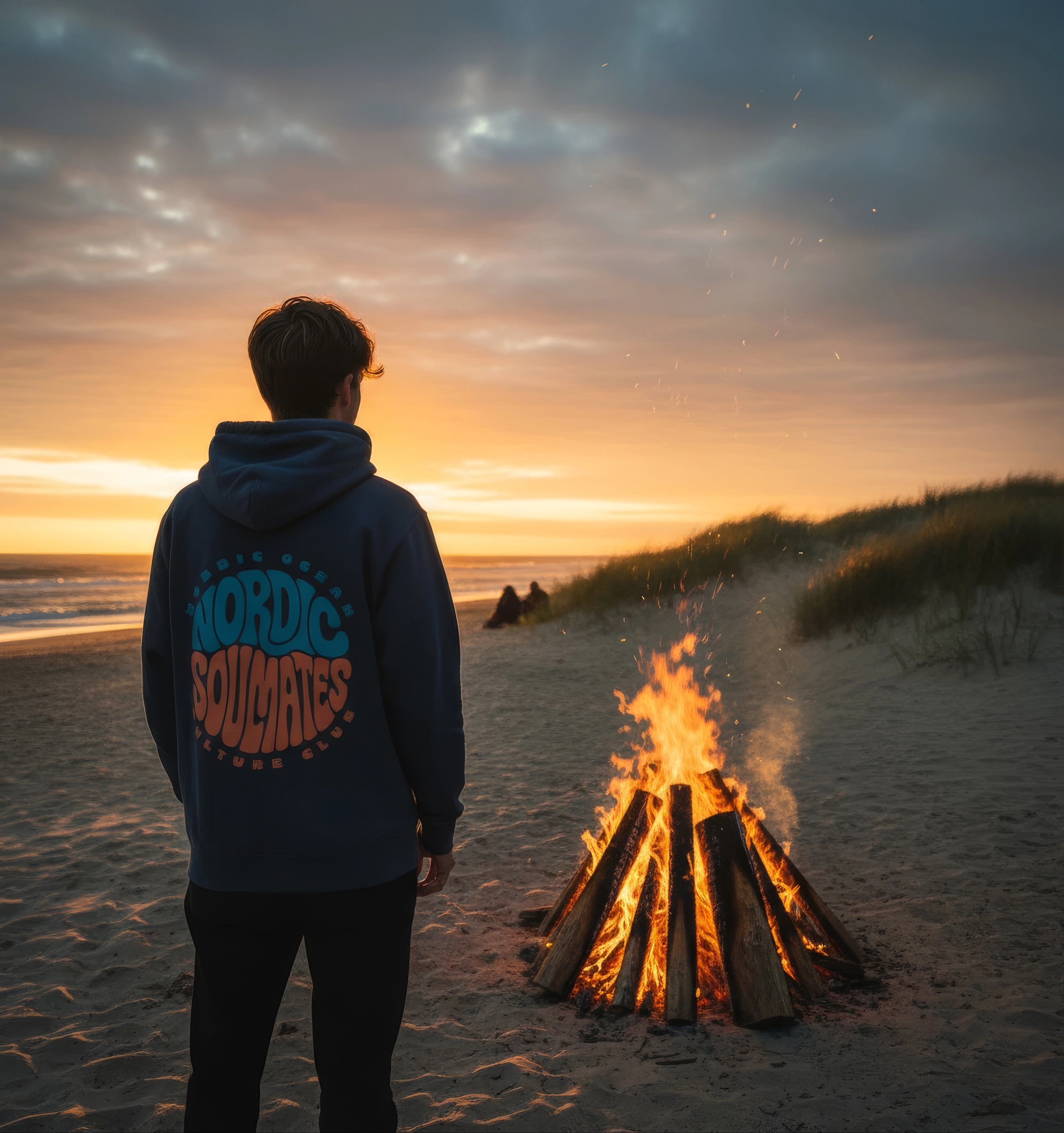 <img src="unity-circle-hoodie-stehend-lagerfeuer.jpg" alt="Mann steht am Strand und trägt den Unisex Nordic Soulmates Unity Circle Hoodie in India Ink Grey: Rückansicht mit großem Backprint, beleuchtet vom flackernden Lagerfeuer, umgeben von nächtlicher Küstenstimmung, gefertigt aus 100% GOTS-zertifizierter Bio-Baumwolle">