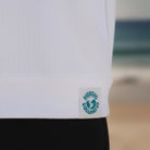 <img src="tide-chaser-hoodie-off-white-webetikett-detail.jpg" alt="Detailaufnahme des Webetiketts am Saum des Tide-Chaser Hoodie in Off-White: GOTS-zertifizierte Bio-Baumwolle, Markenlogo und Pflegehinweise in Nahansicht, gefertigt aus 100% gekämmter, ringgesponnener Bio-Baumwolle">